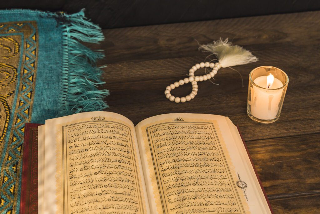 Open Quran with prayer beads, rug, and candle on a table, symbolizing Islamic ethics and trustworthiness in faith.